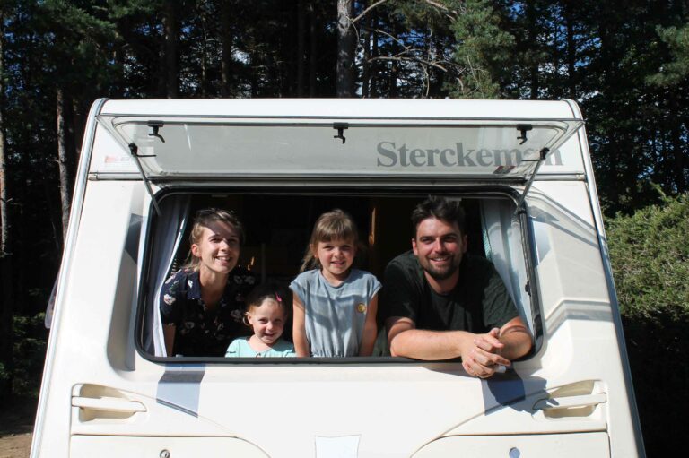 Une famille de quatre personnes souriantes à l'intérieur d’une caravane